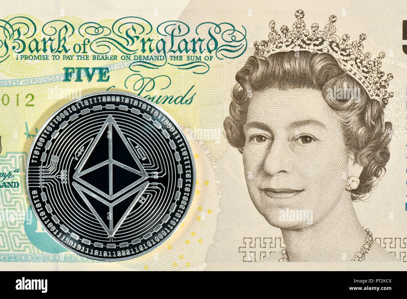 Immagine simbolica di valuta digitale, argento fisico coin Ethereum sulla banconota 5 Inglese Sterline Foto Stock