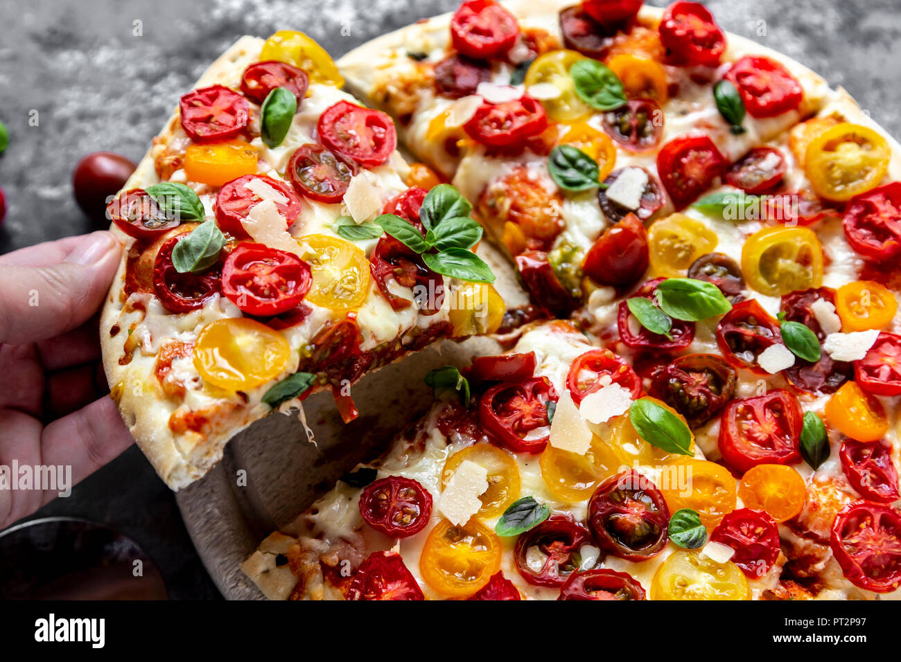 Mano che tiene un trancio di pizza con pomodori e le foglie di basilico Foto Stock