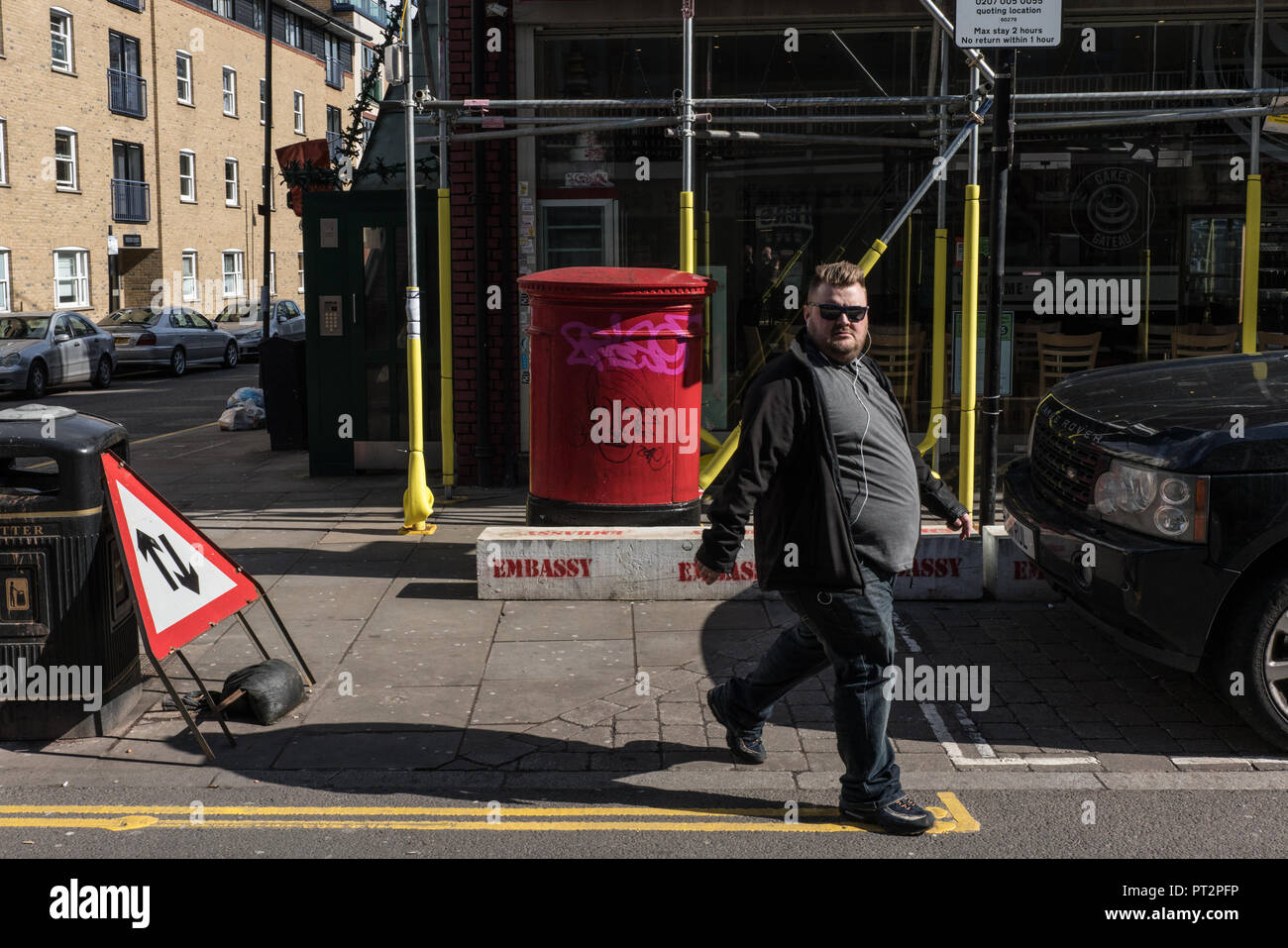 Il maschio sguardi alla macchina fotografica mentre fa la strada su una strada di Londra. Dietro la persona è impalcatura come parte di una rinovazione. Foto Stock