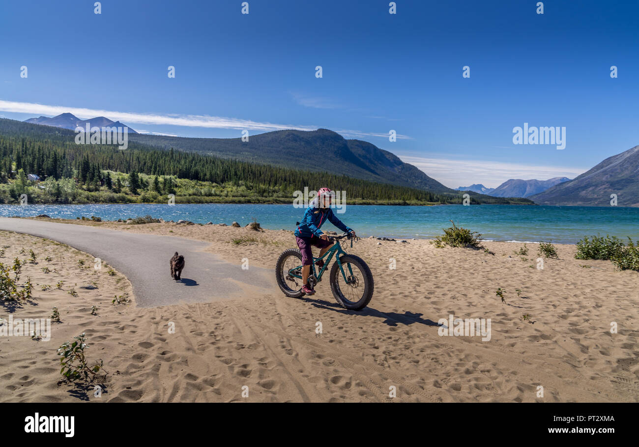 Una donna in bicicletta e a piedi il cane a Benet Lago e spiaggia di Carcross, Yukon Canada Foto Stock