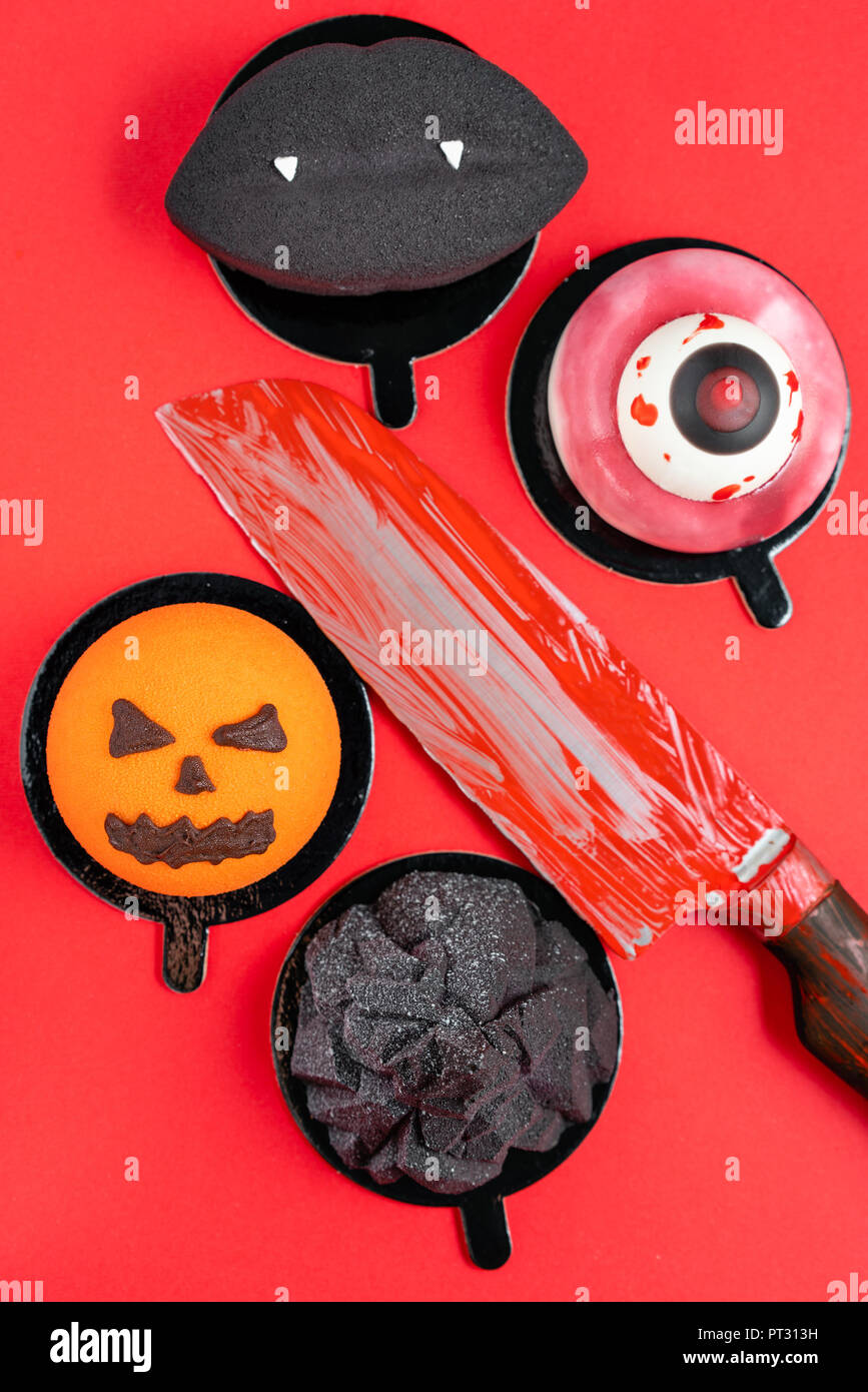 Labbra nere con vampiro canini, strappato un occhio, un infausto di zucca e black mountain. Scary Halloween mousse di zucca su rosso colore di sfondo, vista dall'alto. Il coltello con il sangue Foto Stock