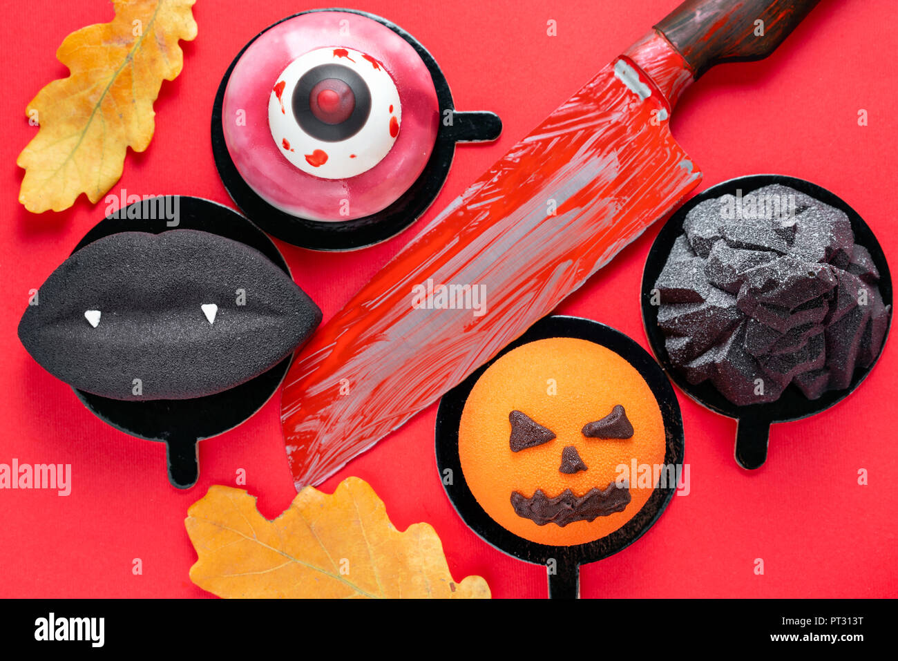 Labbra nere con vampiro canini, strappato un occhio, un infausto di zucca e black mountain. Scary Halloween mousse di zucca su rosso colore di sfondo, vista dall'alto. Il coltello con il sangue Foto Stock