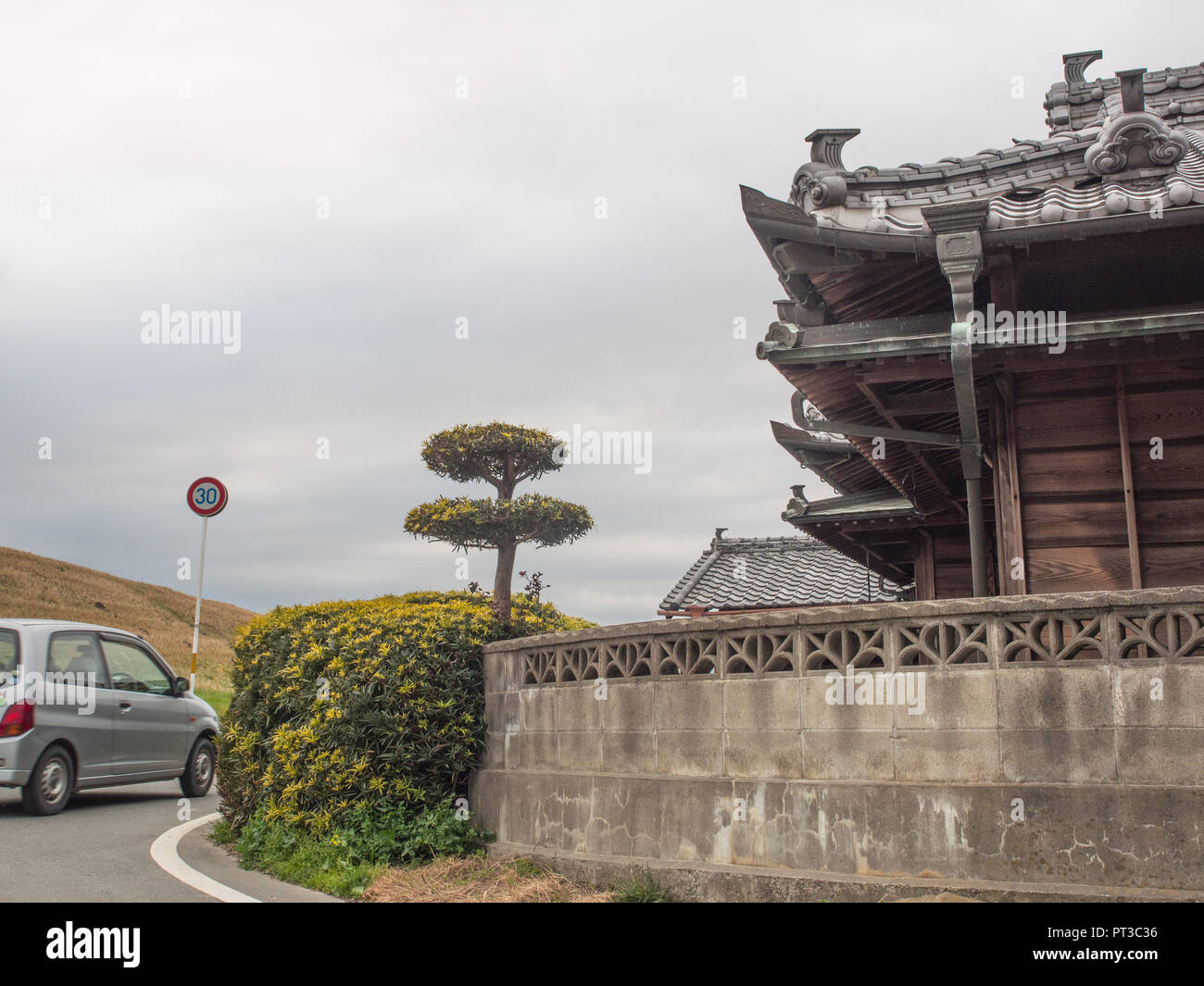 Una vettura che gira intorno a un angolo, road accanto alla tradizionale giapponese del farm house, tetto di tegole con decorazione, una parete incontra una siepe, Yoshino, Takamatsu, Giappone Foto Stock