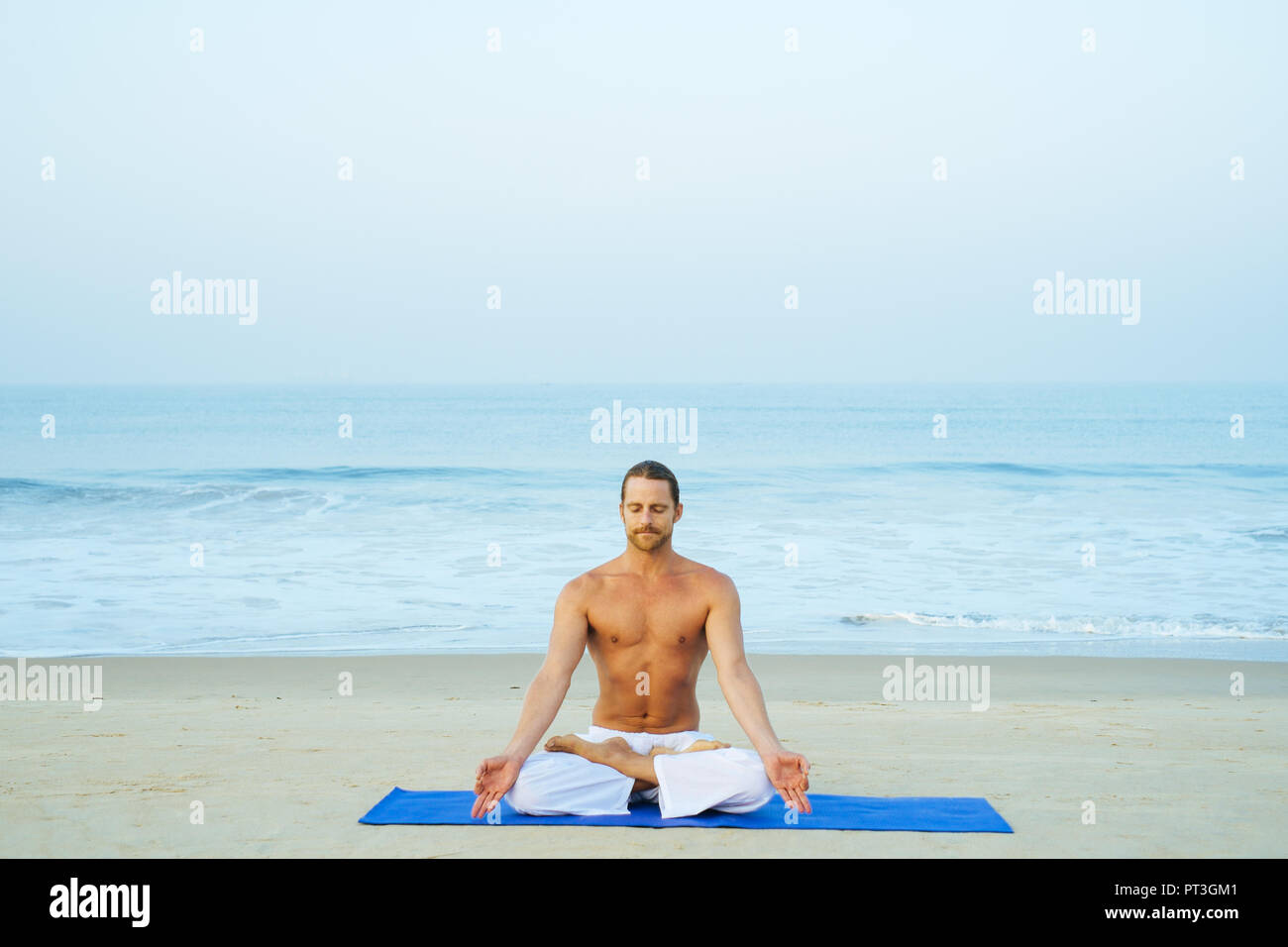 Atletica Giovane uomo che fa joga sulla spiaggia meditare in lotus postura, padmasana Foto Stock