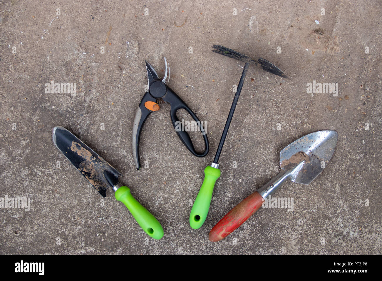 Set di utensili da giardino con maniglie colorate sul pavimento di cemento sullo sfondo Foto Stock