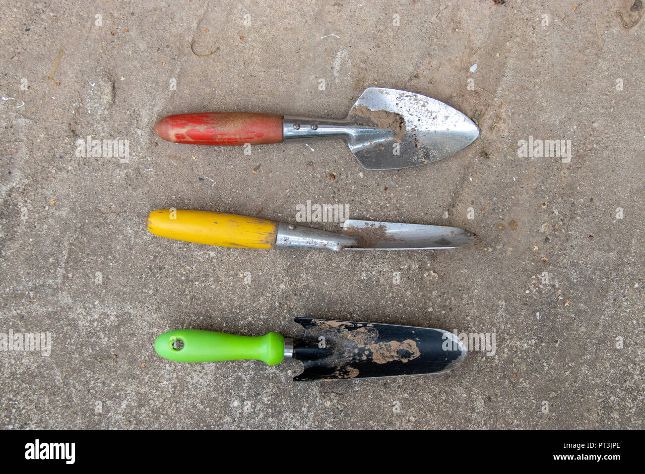 Set di utensili da giardino pale con maniglie colorate sul pavimento di cemento sullo sfondo Foto Stock
