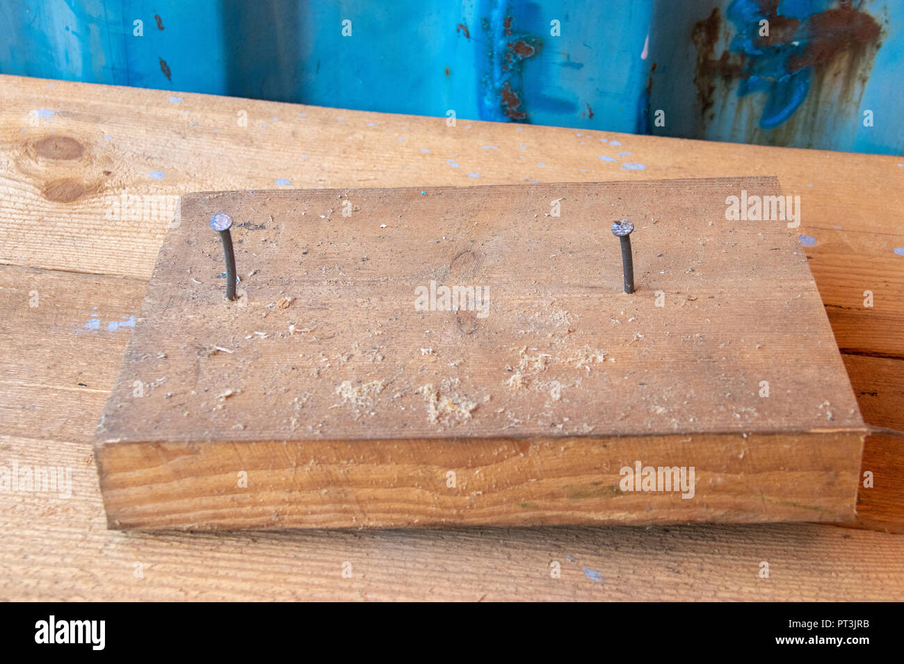 Blocco di legno con due chiodi in officina di riparazione cabinetry banco da lavoro con parete blu Foto Stock