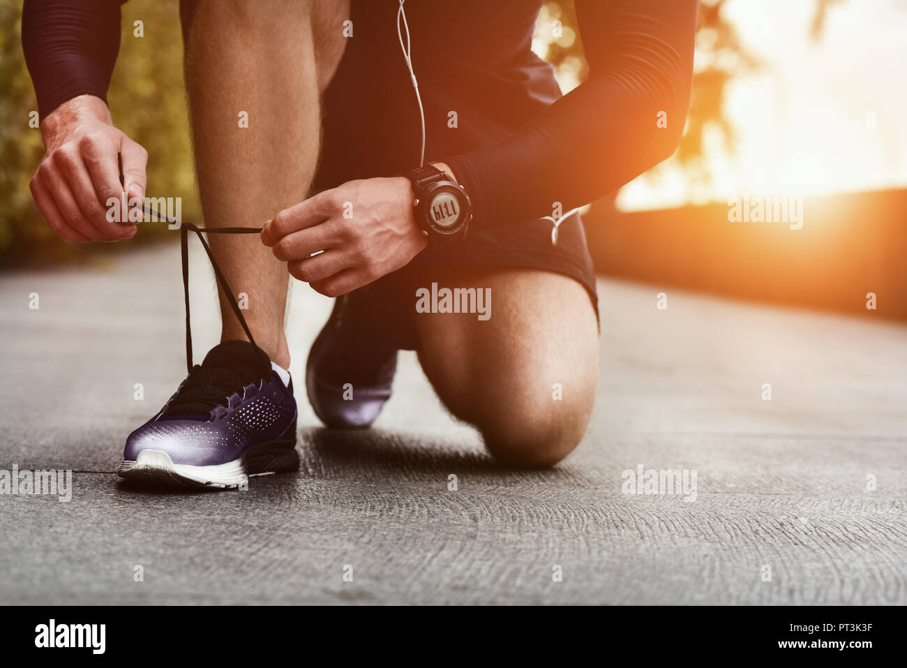 Immagine ritagliata di mani lacci delle scarpe di legatura su sneaker, superficie in esecuzione sullo sfondo. Le mani di uno sportivo con contapassi lacci delle scarpe di legatura su sneaker sportiva. Ru Foto Stock