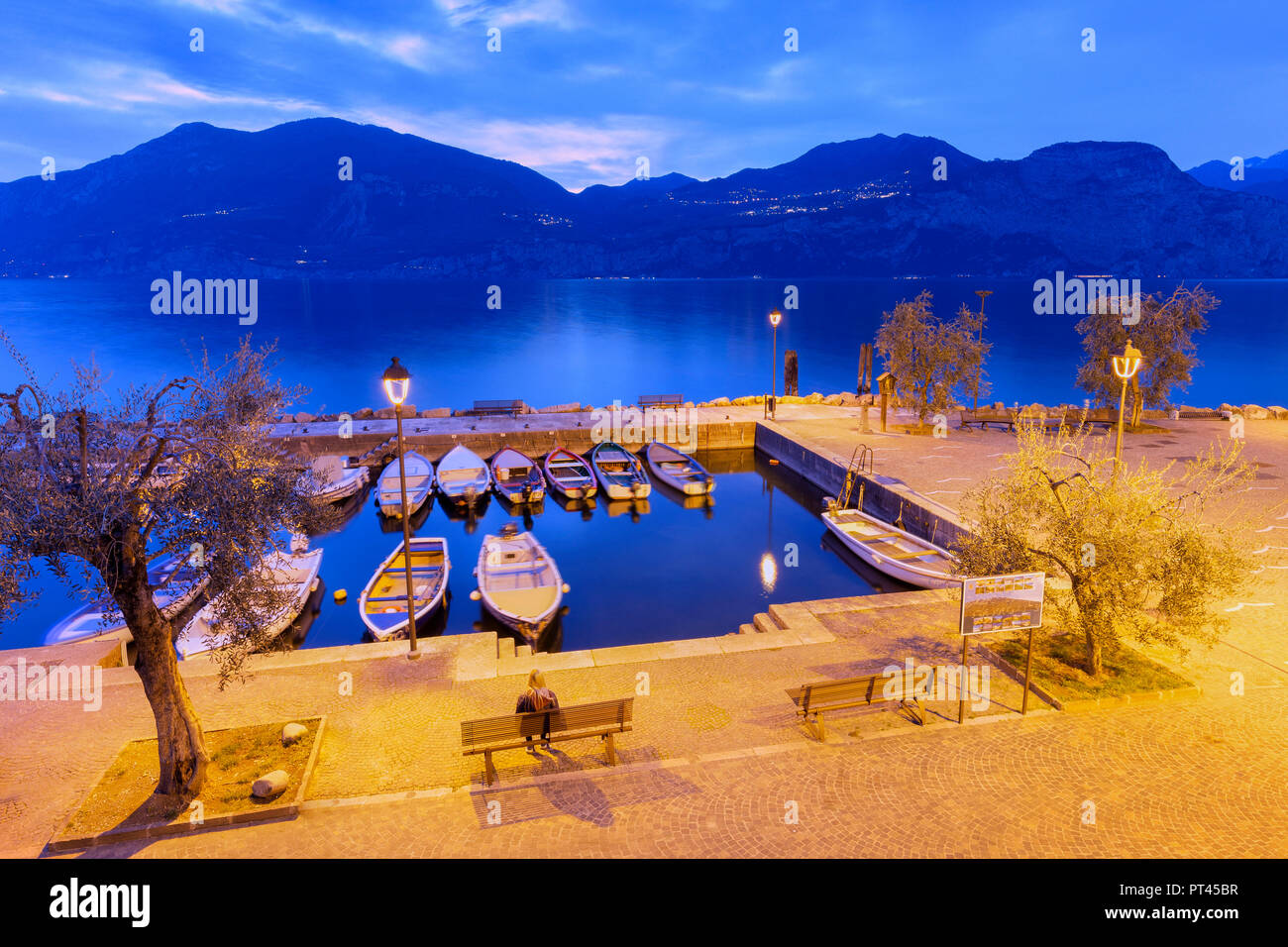 Un turista seduto su una panchina del porto di Macugnano, Brenzone sul Garda Lago di Garda, provincia di Verona, regione Veneto, Italia, Europa Foto Stock