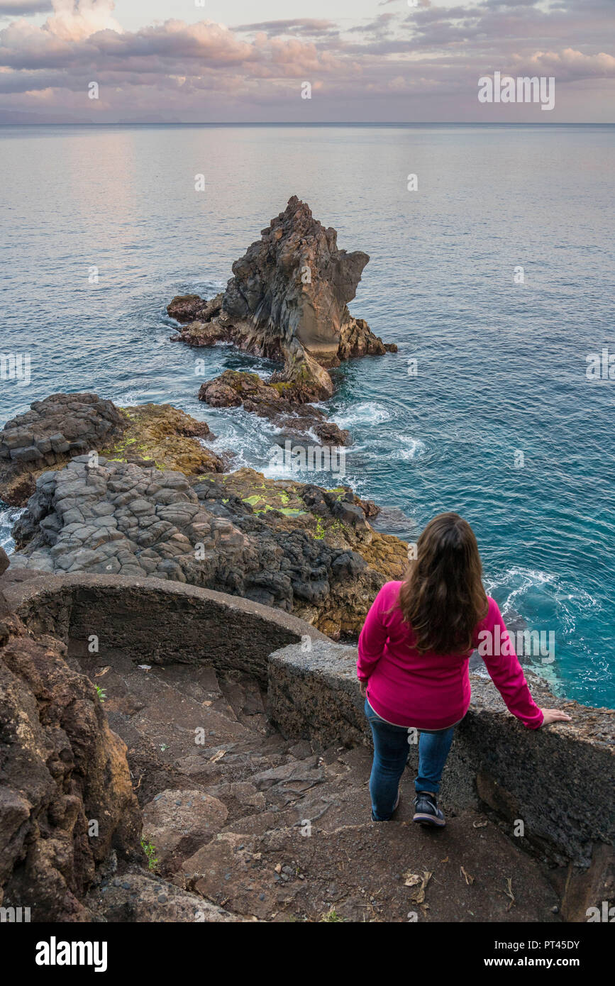 Donna osservando l'Oceano Atlantico e le formazioni rocciose al crepuscolo, Santa Cruz, regione di Madera, Portogallo, Foto Stock