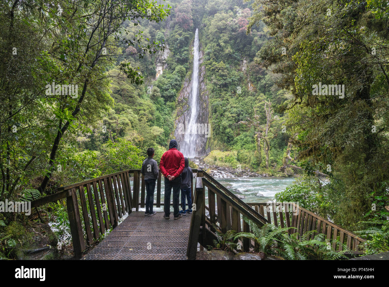 Turisti sotto la pioggia ammirando Thunder Creek Falls, montare gli aspiranti National Park, West Coast, regione di South Island, in Nuova Zelanda, Foto Stock