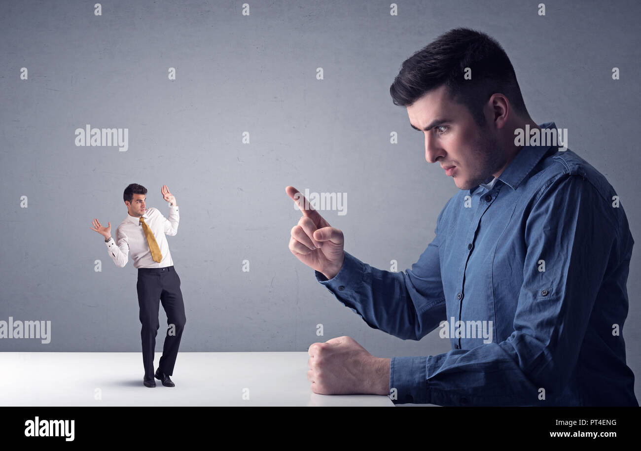 Giovane imprenditore professionale essendo arrabbiato con un altro imprenditore in miniatura di fronte a uno sfondo grigio Foto Stock