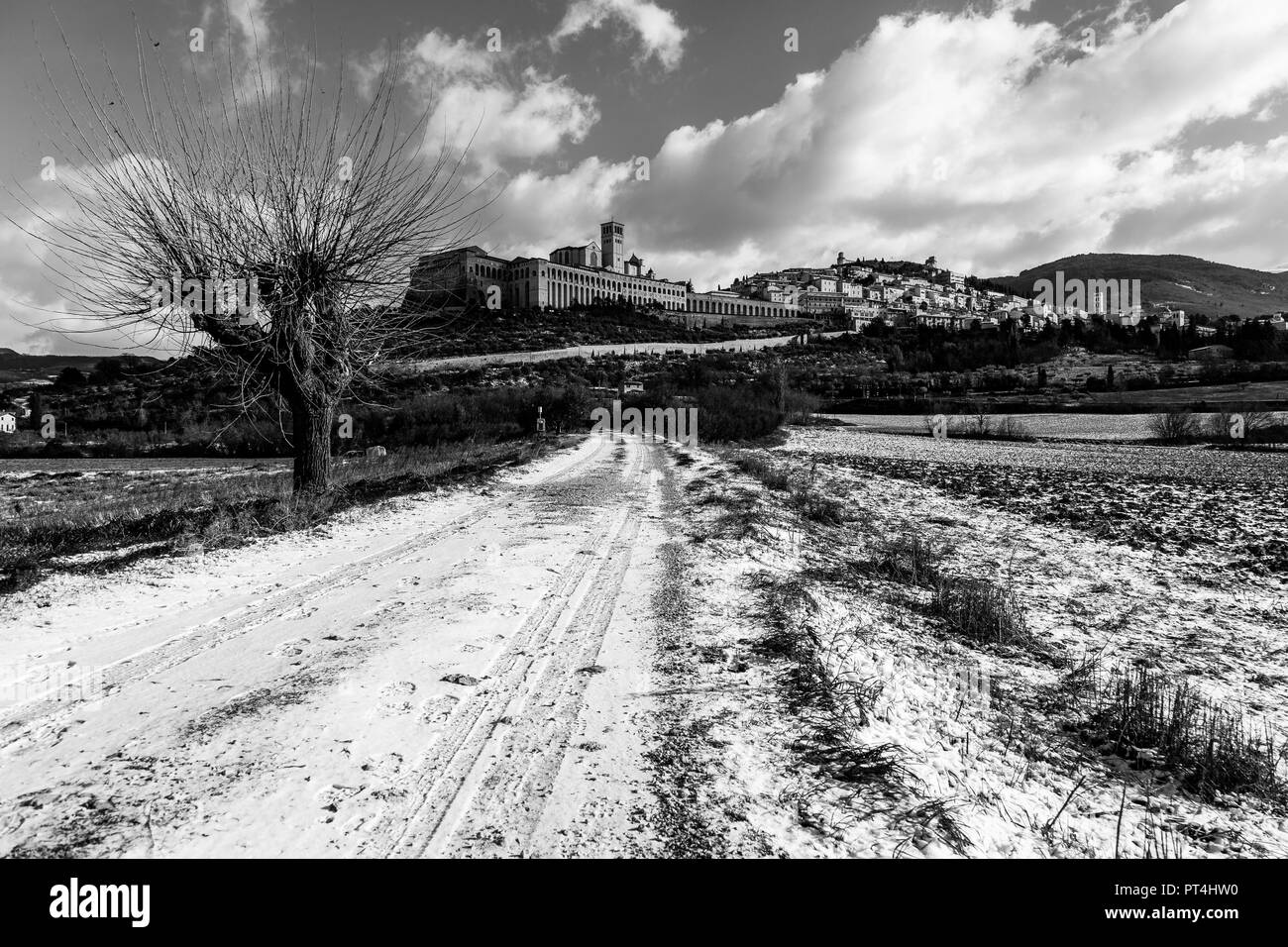 Vista della città di Assisi (Umbria) in inverno, con un paese di strade coperte da neve e cielo con nuvole bianche Foto Stock