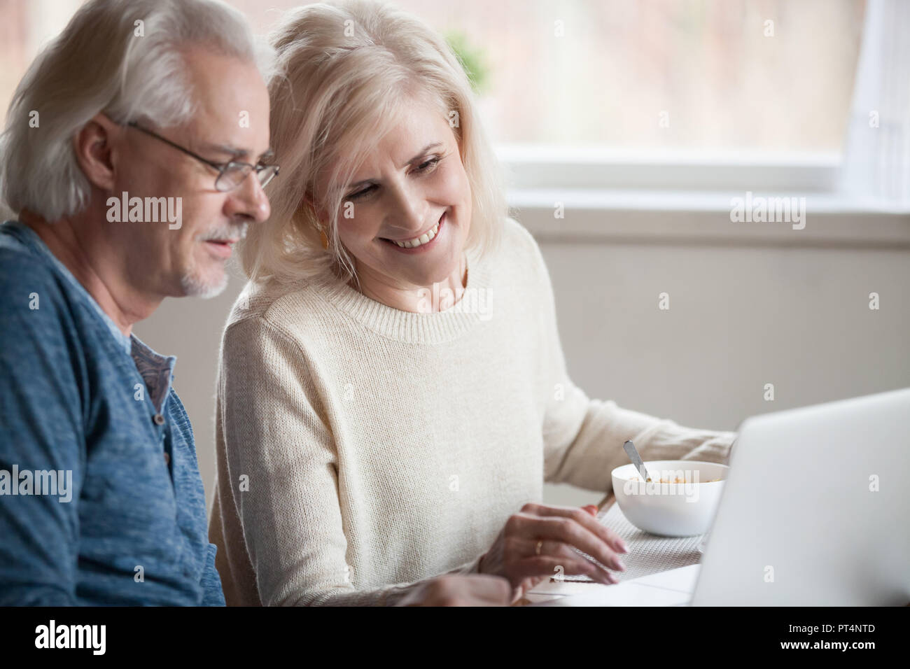 Senior coppia felice godendo utilizzando laptop mangiare insieme per la prima colazione, sorridente centro anziani di età compresa tra famiglia shopping online, la lettura di discutere di internet n Foto Stock