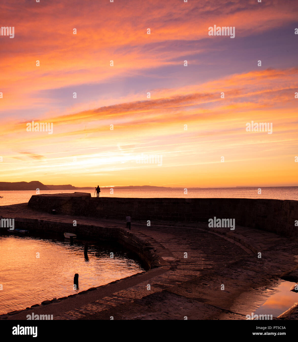 Lyme Regis, Dorset, Regno Unito. Il 7 ottobre 2018. Regno Unito Meteo: Un fotografo cattura la scena come il cielo sopra il porto di Cobb glow con colori vibranti all'inizio di una luminosa e soleggiata giornata autunnale a Lyme Regis. Credito: Celia McMahon/Alamy Live News Foto Stock