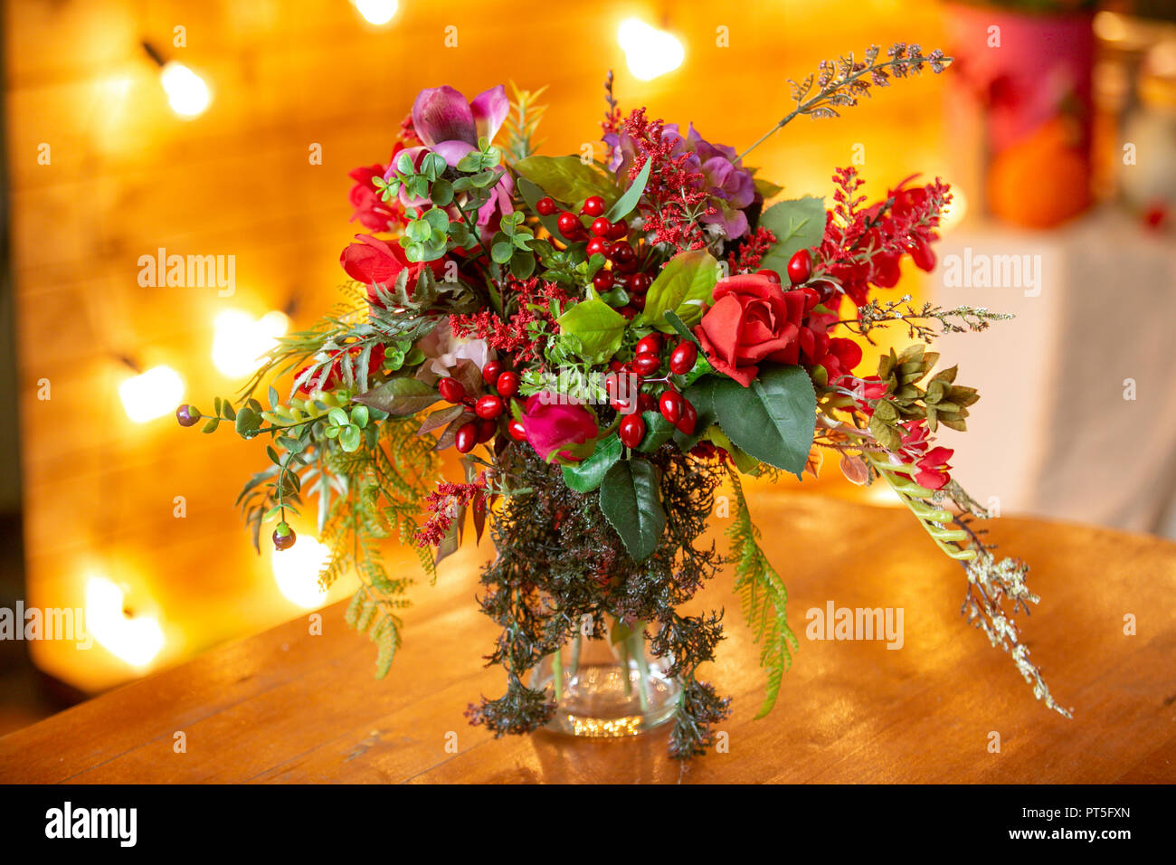 Composizione floreale con bacche rosse, rose rosse e verdi sul tavolo Foto Stock