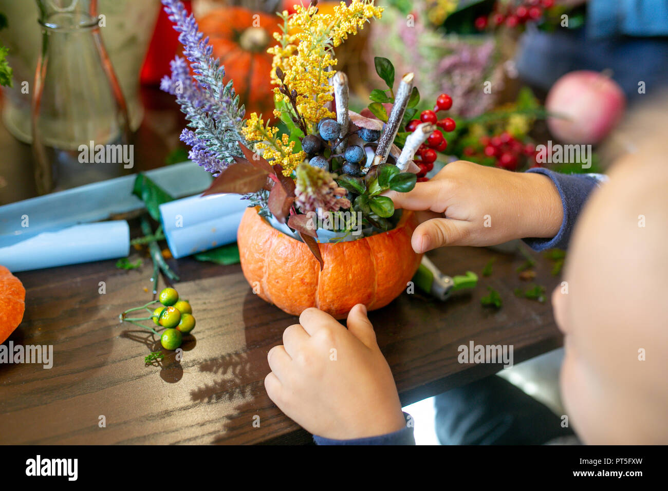 Un bambino rende un omaggio floreale in una zucca sul tavolo Foto Stock