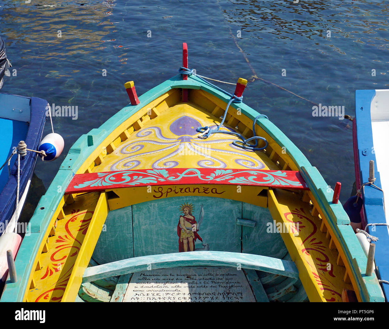 Verniciato colorato barca da pesca con testo religioso al porto del villaggio di pescatori di Aci Trezza, comune di Aci Castello, Catania, Sicilia, Italia Foto Stock