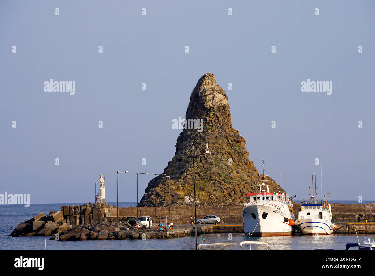 Barche da pesca al porto di Aci Trezza, dietro la roccia di basalto Faraglione grande, Isole dei Ciclopi, comune di Aci Castello, Catania, Sicilia, Ita Foto Stock