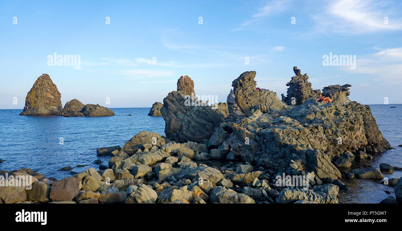 Persone su una roccia di basalto presso le isole dei Ciclopi, Aci Trezza, comune di Aci Castello, Catania, Sicilia, Italia Foto Stock