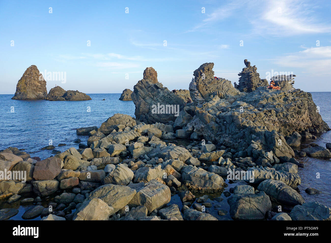 Persone su una roccia di basalto presso le isole dei Ciclopi, Aci Trezza, comune di Aci Castello, Catania, Sicilia, Italia Foto Stock