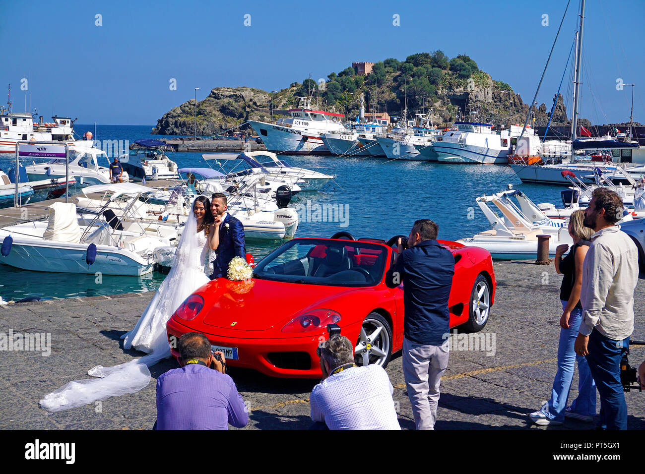 Sessione fotografica, coppia di sposi con la Ferrari al porto di Aci Trezza, dietro l'isola Lachea, isola principale del ciclope, Catania, Sicilia, Italia Foto Stock
