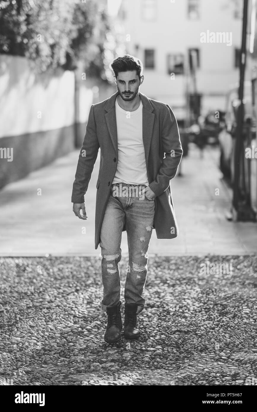 Giovane uomo che indossa abbigliamento invernale in strada. Giovane ragazzo barbuto con moderni acconciatura con rivestimento, jeans blu e bianca t-shirt. Foto Stock