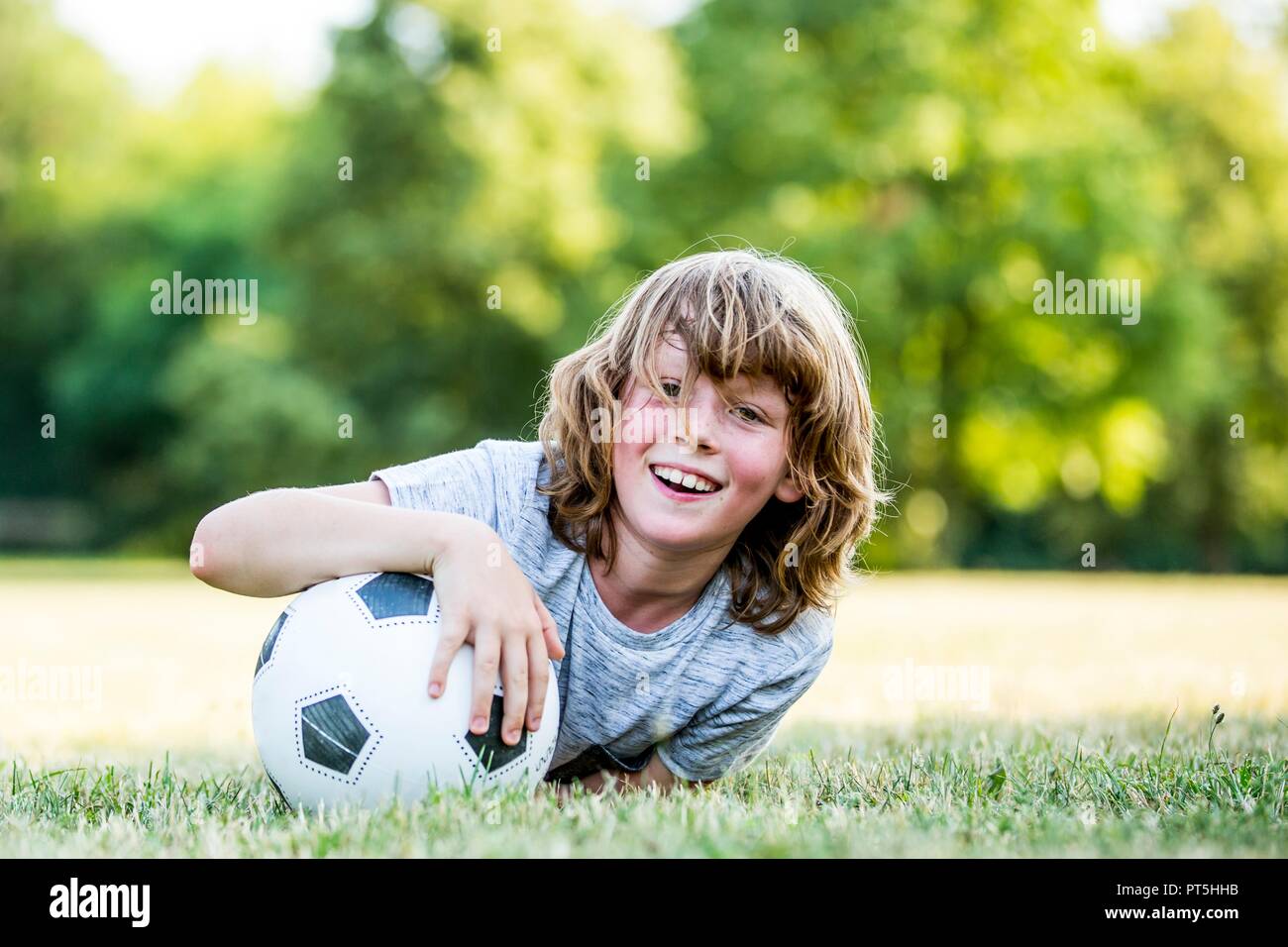 Ragazzo tenendo il calcio mentre giaceva nel parco, sorridente, ritratto. Foto Stock