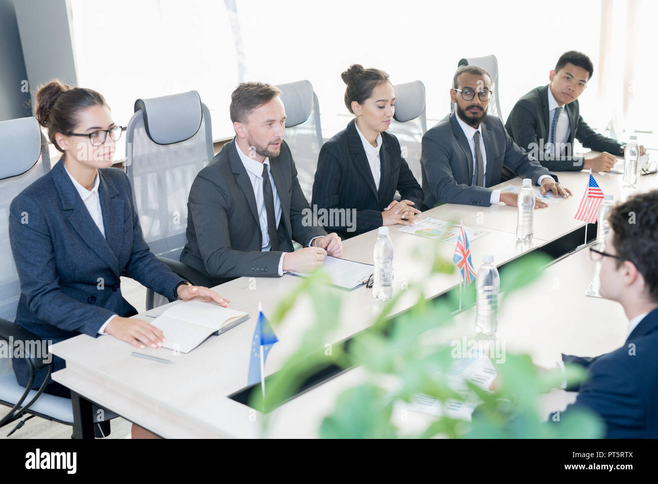 Gruppo di certi rappresentanti dei paesi in convenzionale seduto in fila al tavolo da conferenza con le bandiere nazionali e documenti e che conduce i negoziati Foto Stock