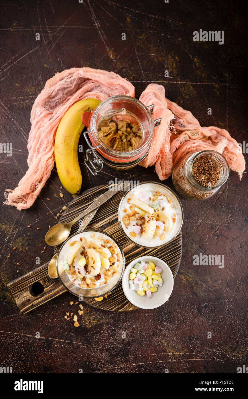 Una sana dolce fatto di yogurt e una banana, granola e i dadi su un tondo in legno tagliere su uno sfondo scuro. Vista superiore Foto Stock