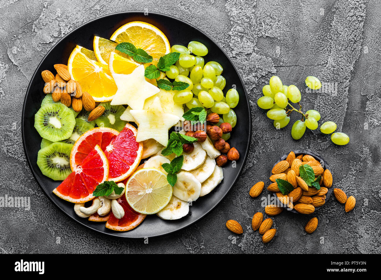 Sana ciotola vegetariano piatto con frutta fresca e i dadi. Piastra con raw apple, arancia, pompelmo, banana, kiwi, limone, uva e dadi Foto Stock