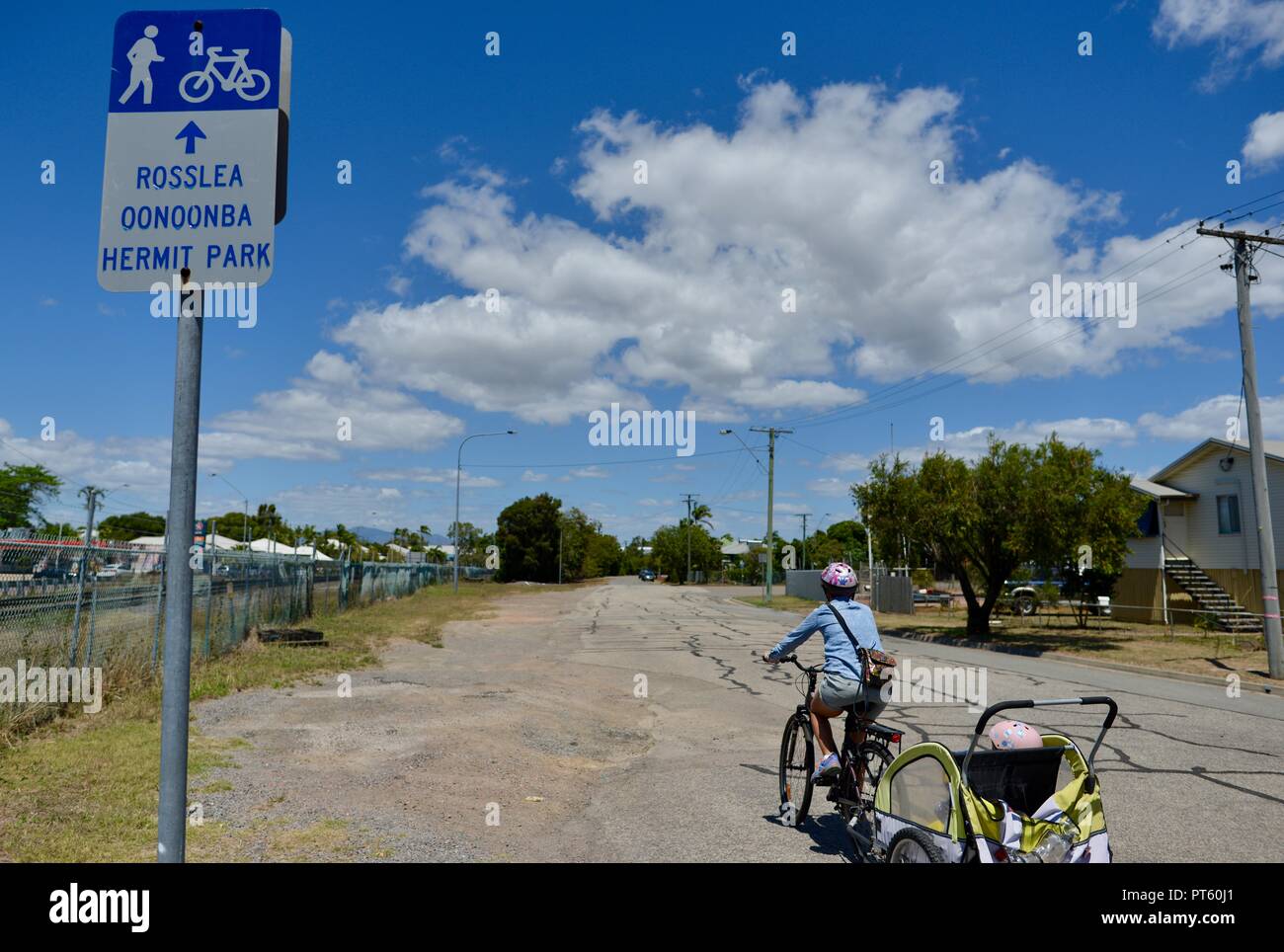 La donna in sella ad una bicicletta con un rimorchio per biciclette per bambini, Townsville, QLD, Australia Foto Stock