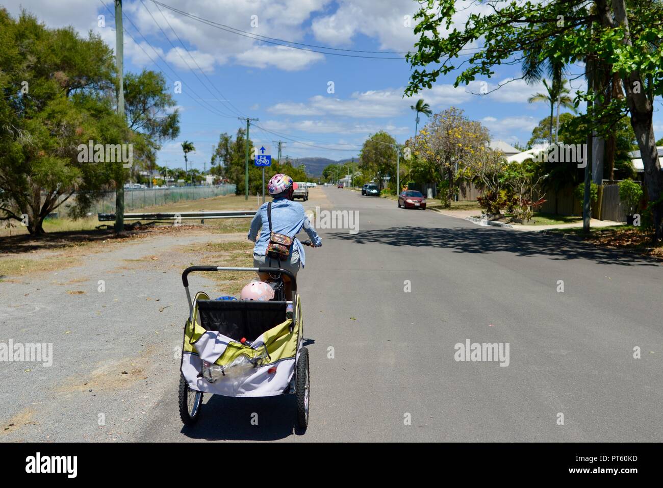 La donna in sella ad una bicicletta con un rimorchio per biciclette per bambini, Townsville, QLD, Australia Foto Stock