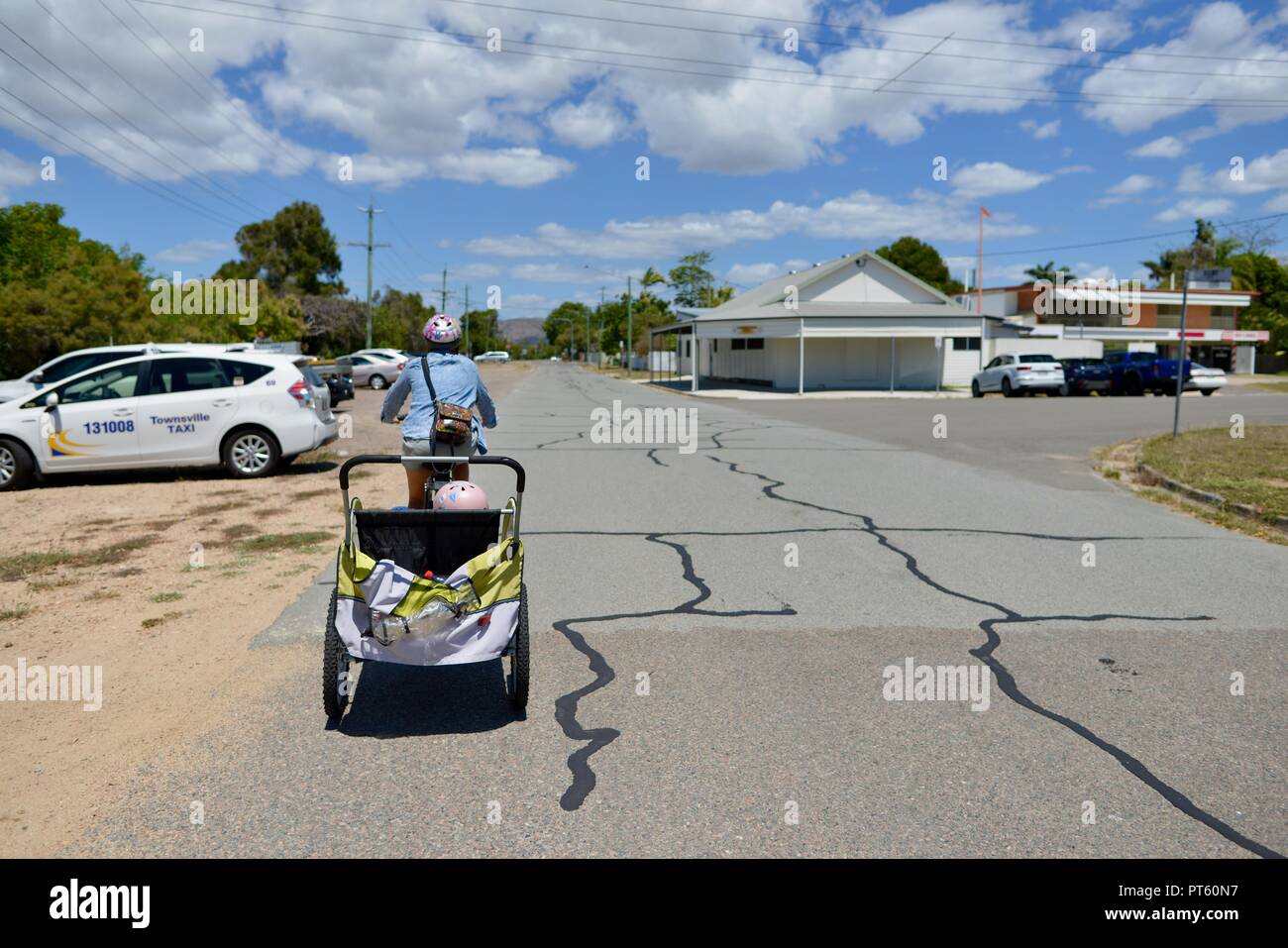 La donna in sella ad una bicicletta con un rimorchio per biciclette per bambini, Townsville, QLD, Australia Foto Stock
