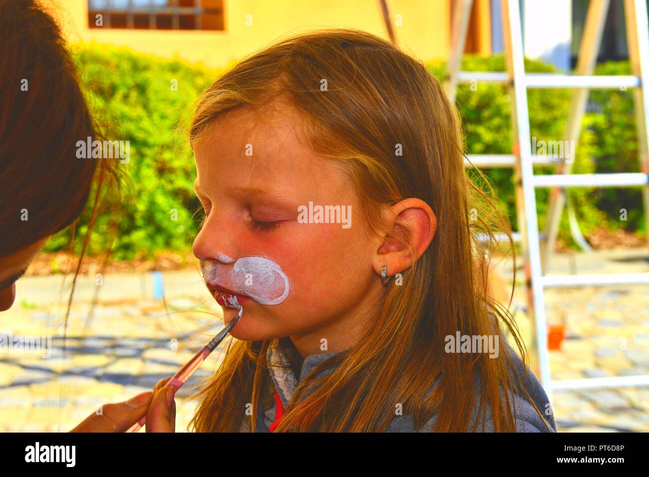 La donna faccia la pittura di capretto all'esterno. Baby face painting. Bambina ottenendo il suo volto dipinto come un coniglio dal volto dipinto artista. Foto Stock