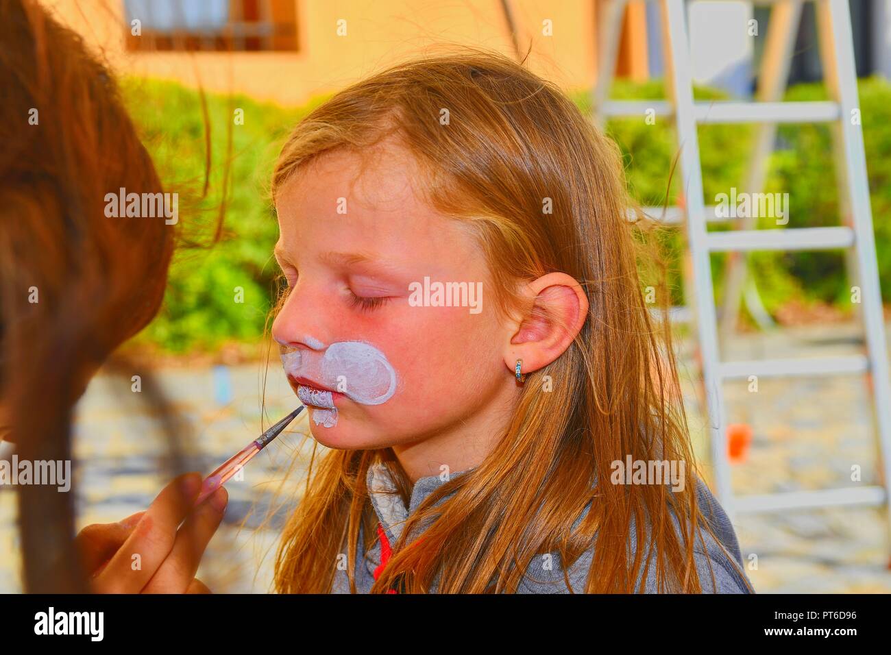 La donna faccia la pittura di capretto all'esterno. Baby face painting. Bambina ottenendo il suo volto dipinto come un coniglio dal volto dipinto artista. Foto Stock