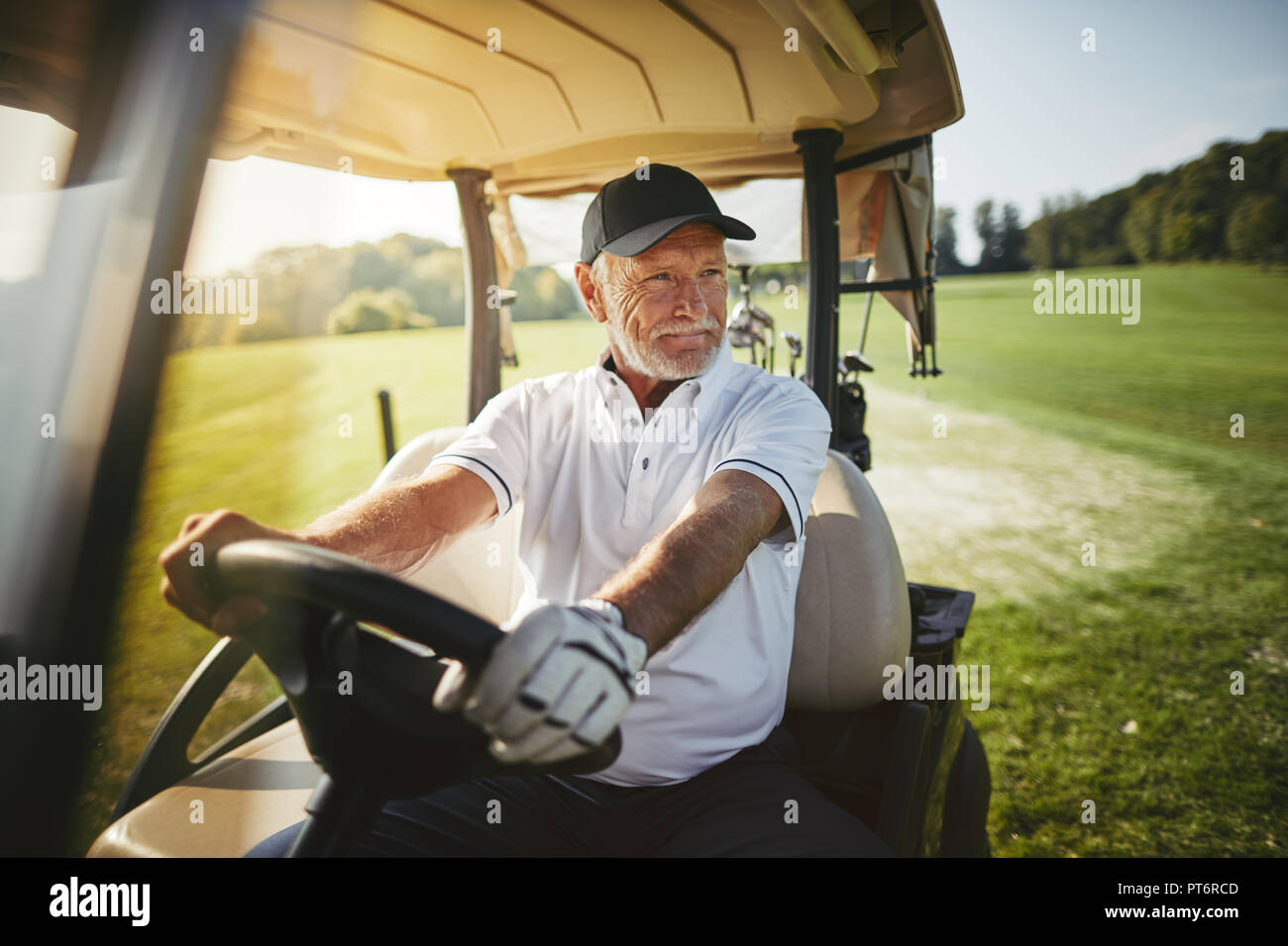 Senior sorridente uomo alla guida di un carrello da golf lungo un corso mentre godendo di un round di golf in una giornata di sole Foto Stock