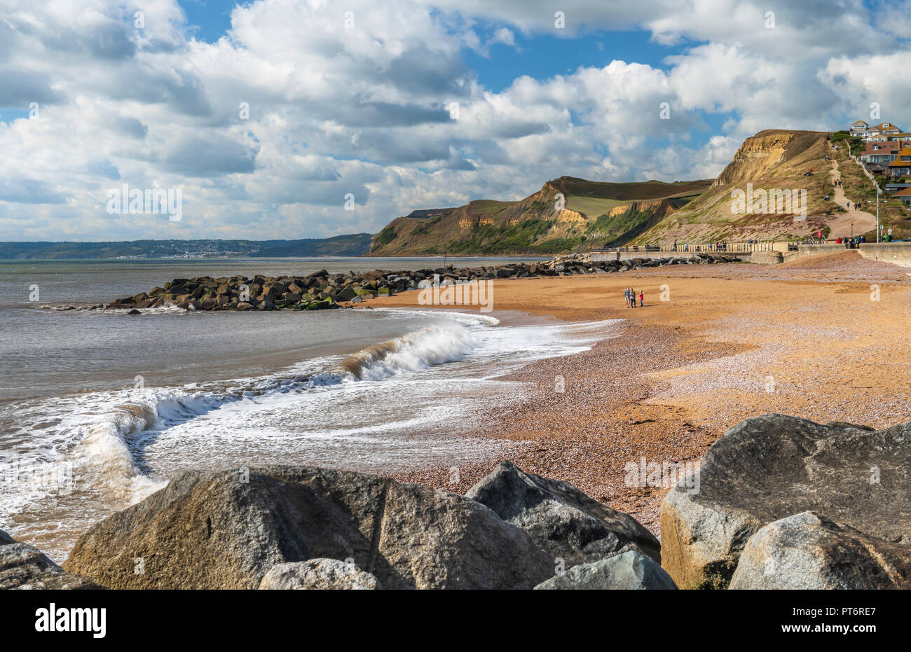 In un pomeriggio soleggiato sulla Jurassic Coast, una famiglia guarda le onde si infrangono sulla bella spiaggia di West Bay nel Dorset. Foto Stock