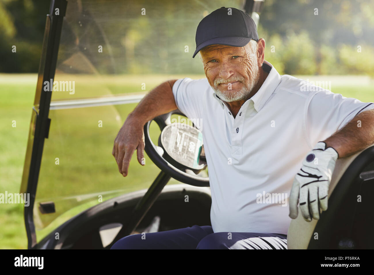 Senior uomo sorridente mentre è seduto in un carrello godendo di un round di golf in una giornata di sole Foto Stock