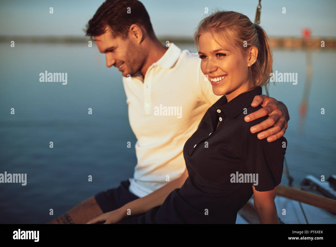 Sorridente coppia giovane seduto a braccetto insieme sul ponte del loro yacht mentre godendo una giornata di sole in barca a vela Foto Stock