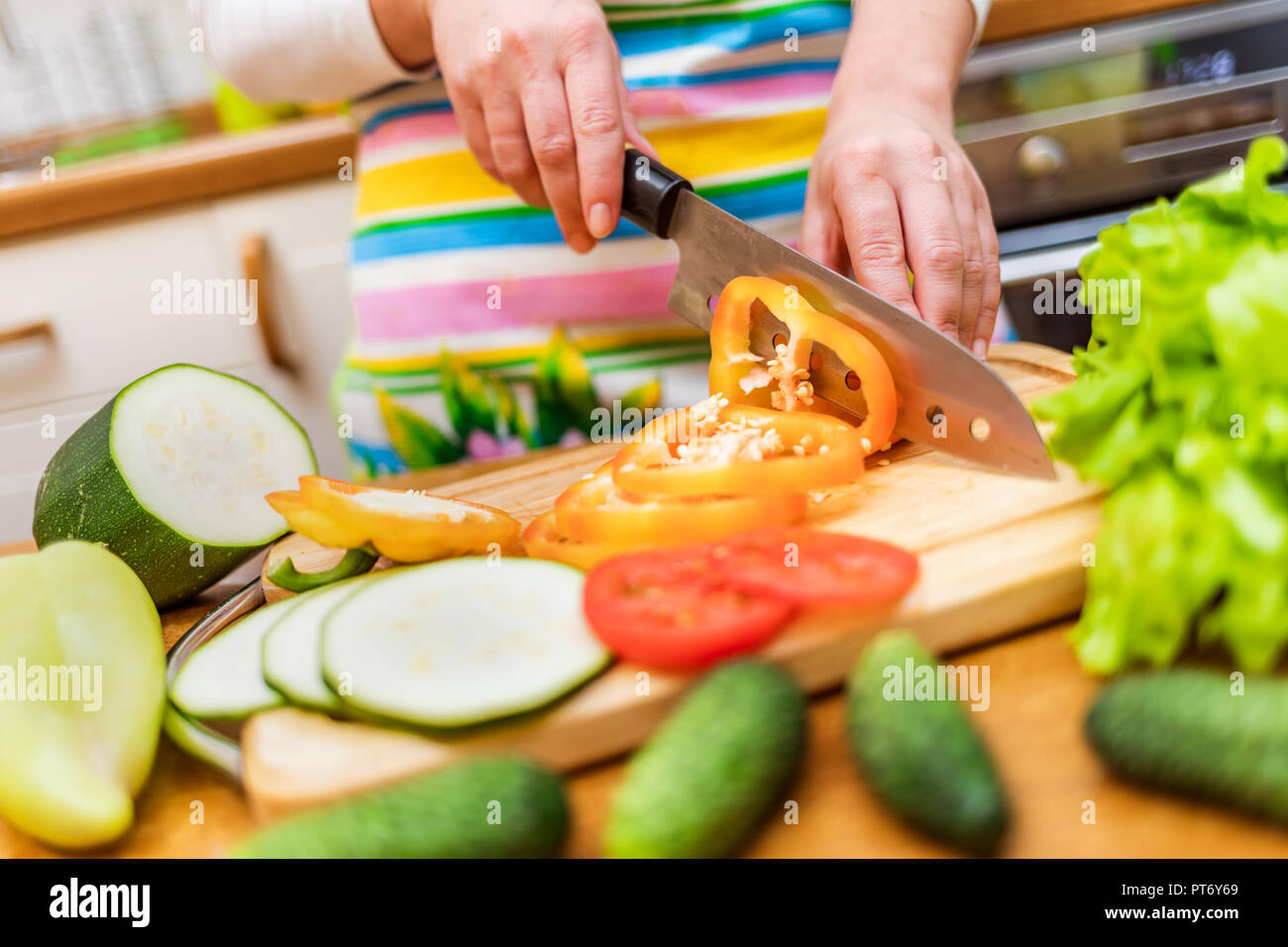 Mani femminili di casalinga con un coltello tagliare freschi il peperone sul tagliere tavolo da cucina Foto Stock