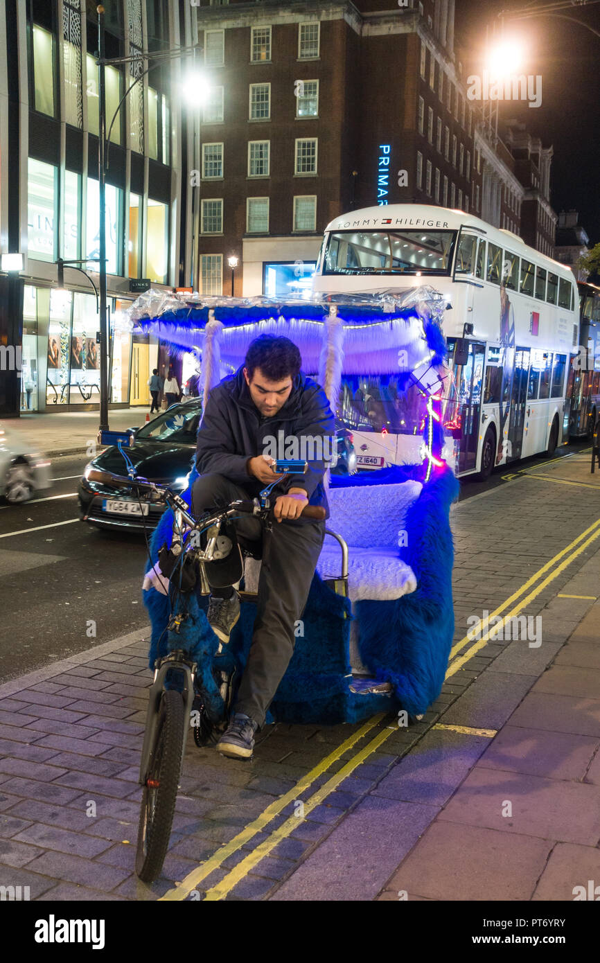 Noleggio taxi parcheggiato al tramonto su una strada di Londra mentre il pilota usa il suo telefono cellulare. Foto Stock