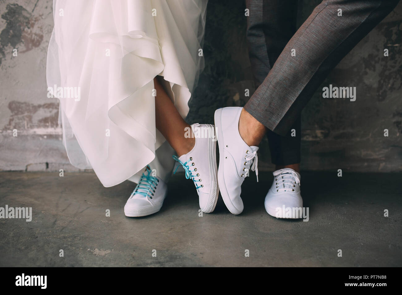 Ritagliato maschio e femmina gambe indossando sneakers bianco. Nozze in sneakers Foto Stock
