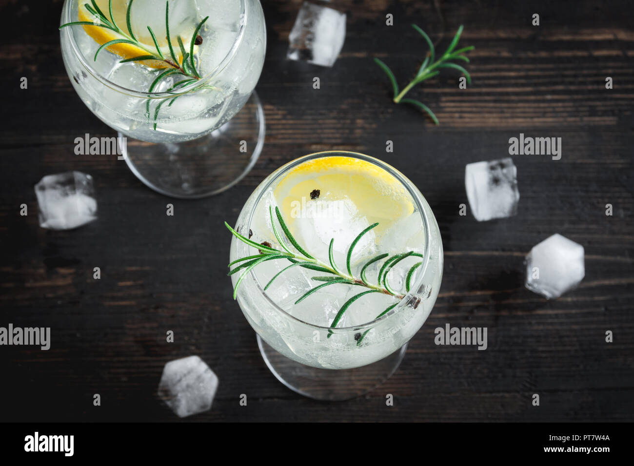 Bere alcool (gin tonic cocktail) con limone e rosmarino e ghiaccio su rustiche tavoli in legno nero, copia spazio, vista dall'alto. Iced cocktail drink con limone e Foto Stock