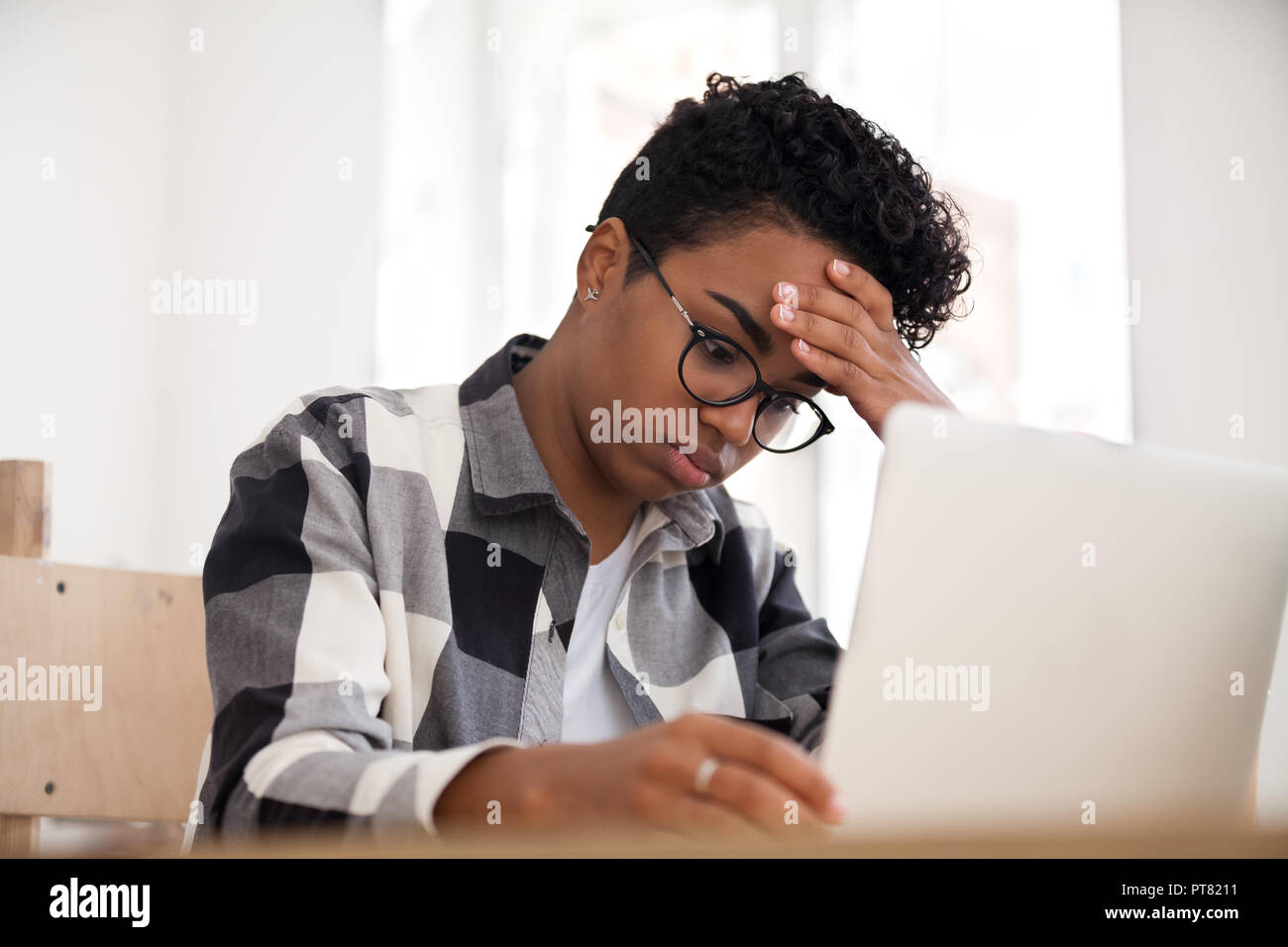 Sconvolto american donna seduta a lavorare utilizzando computer portatile in ufficio Foto Stock