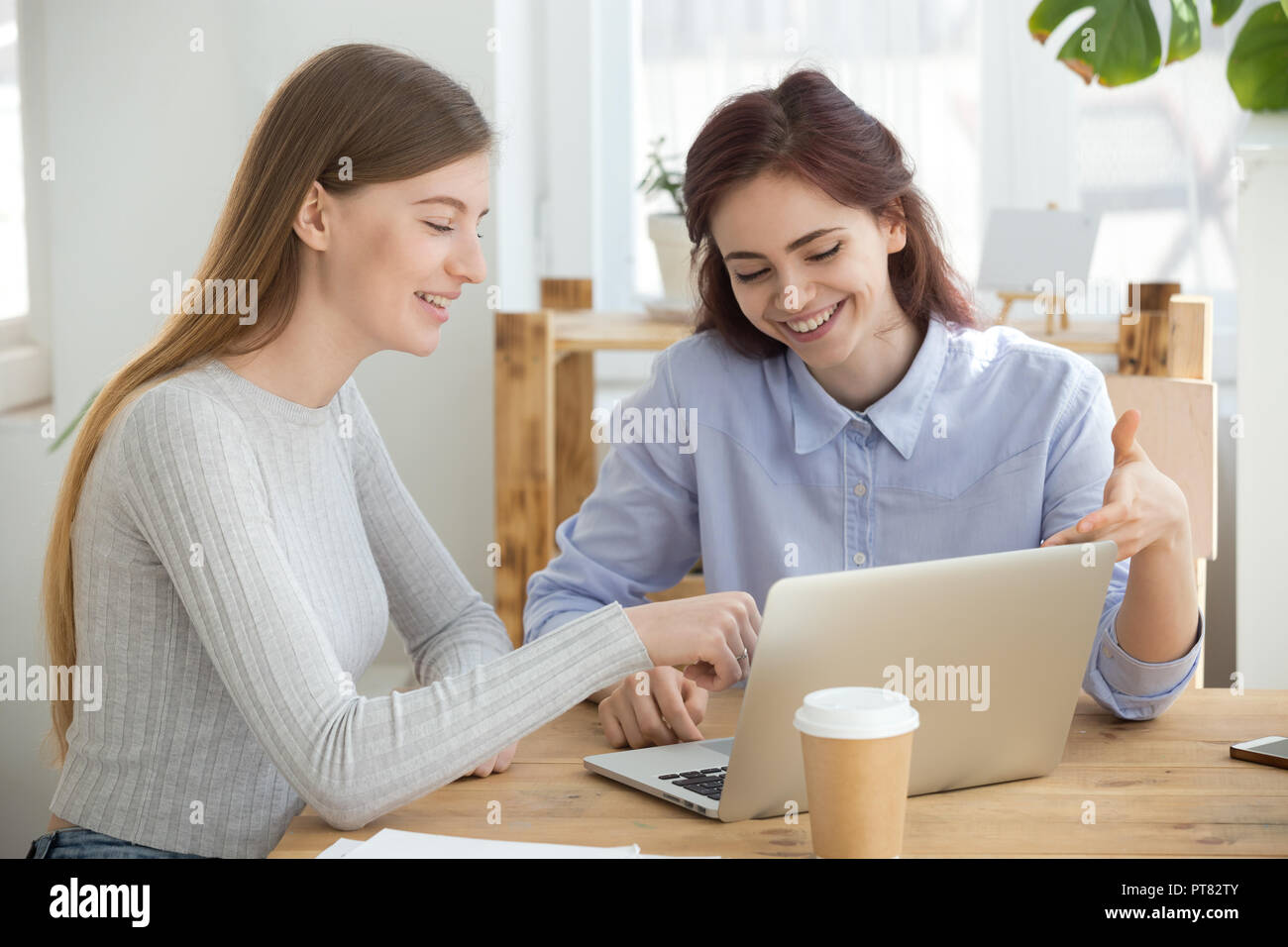 La millenaria donne guardando al computer seduta sorridente in ufficio Foto Stock