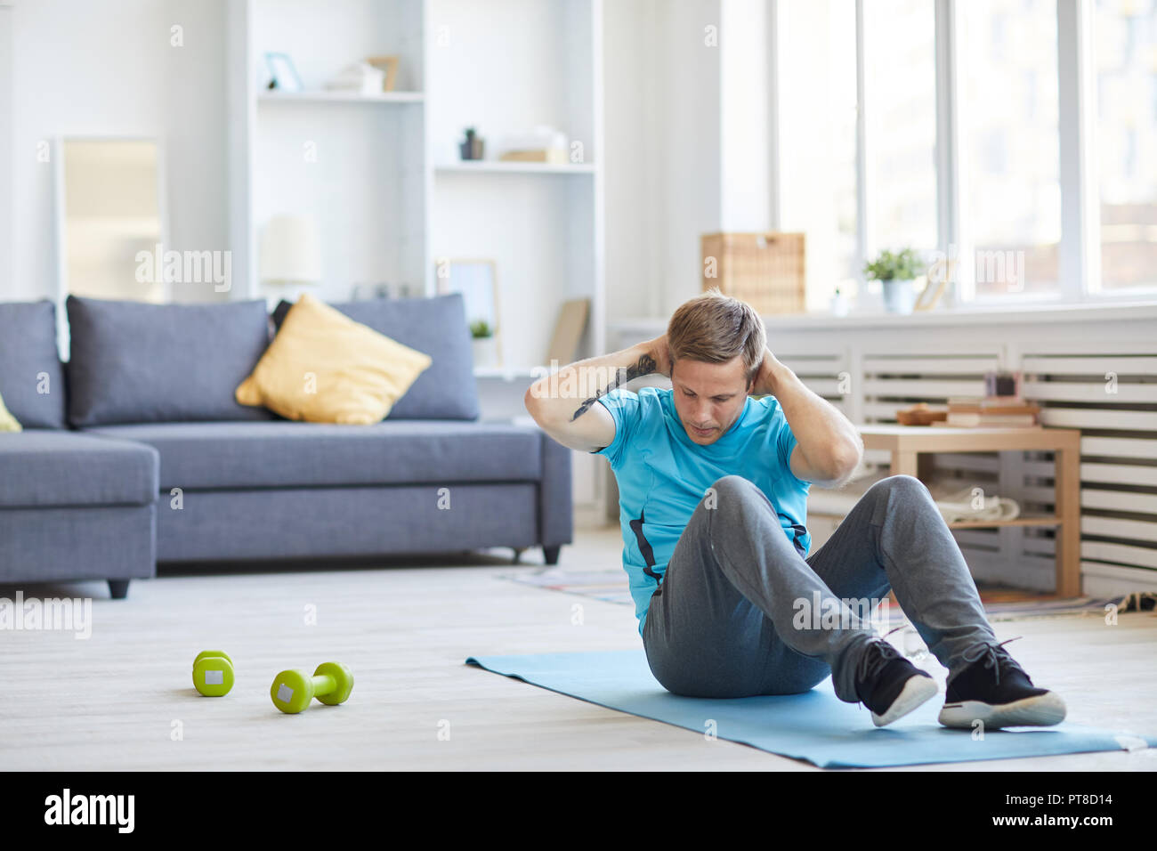 Giovane activewear seduto sul pavimento con le mani dietro la testa e facendo sit ups Foto Stock