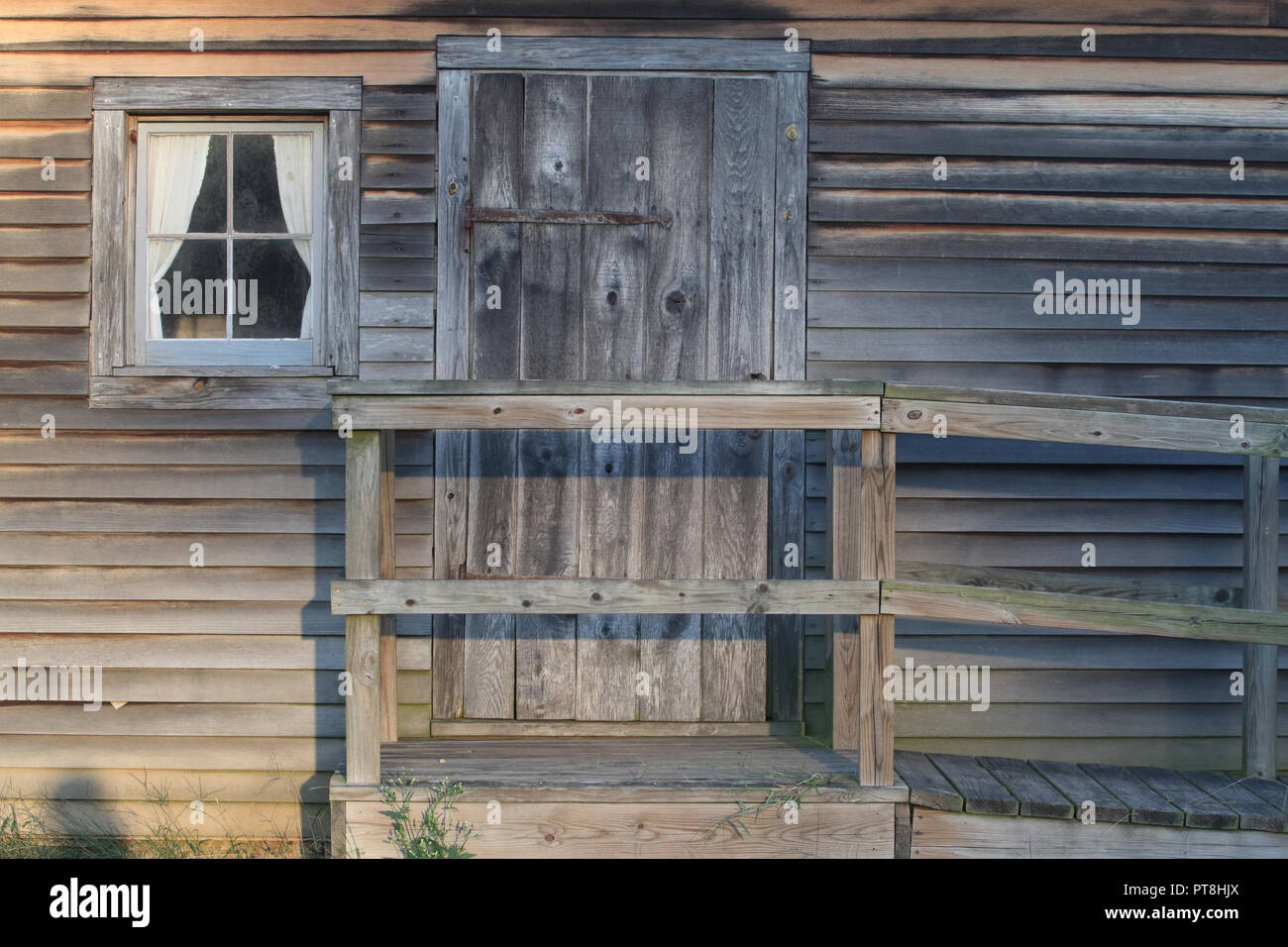 Un ingresso rustico di legno vecchio cabina con clapboard incompiuta di parteggiare per una finestra, una porta e una acquasantiera con rampa e corrimano. Foto Stock