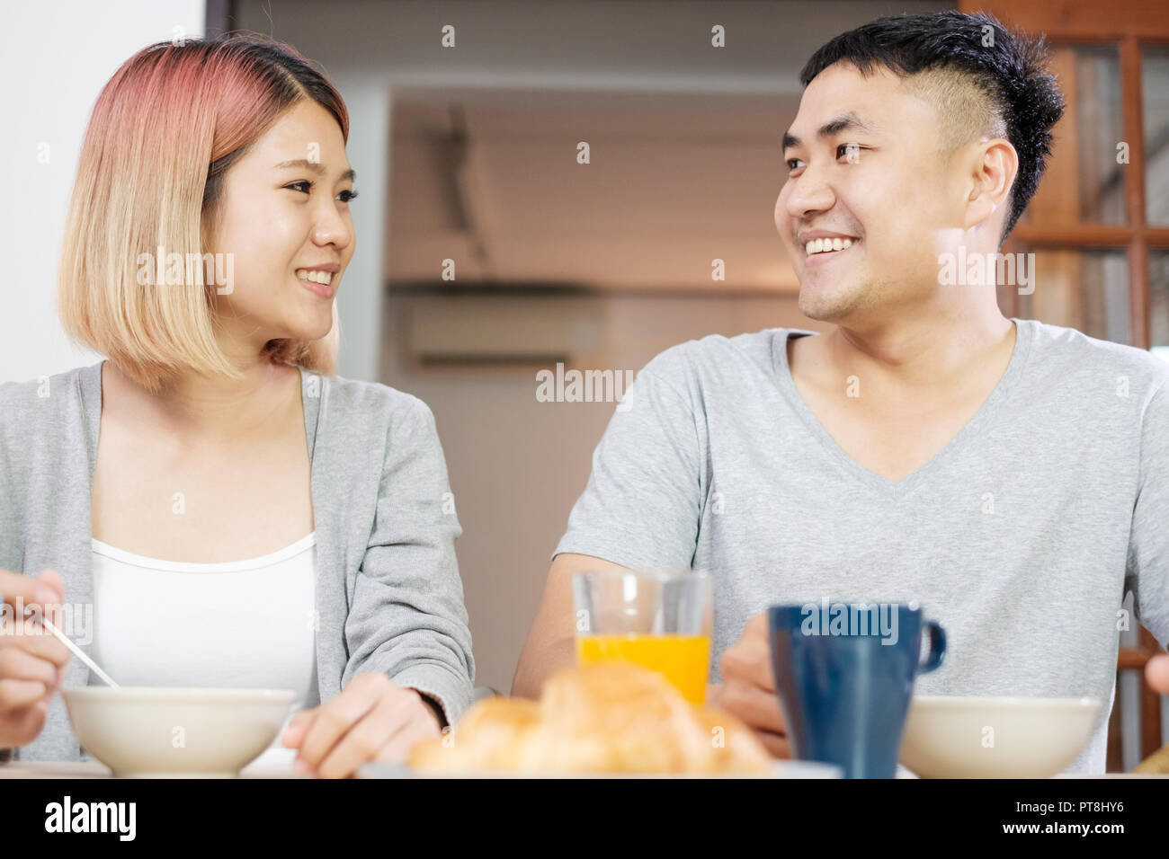 Felice coppia asiatica in pigiama seduta a tavola in cucina a casa la mattina e avente cereale colazione insieme Foto Stock