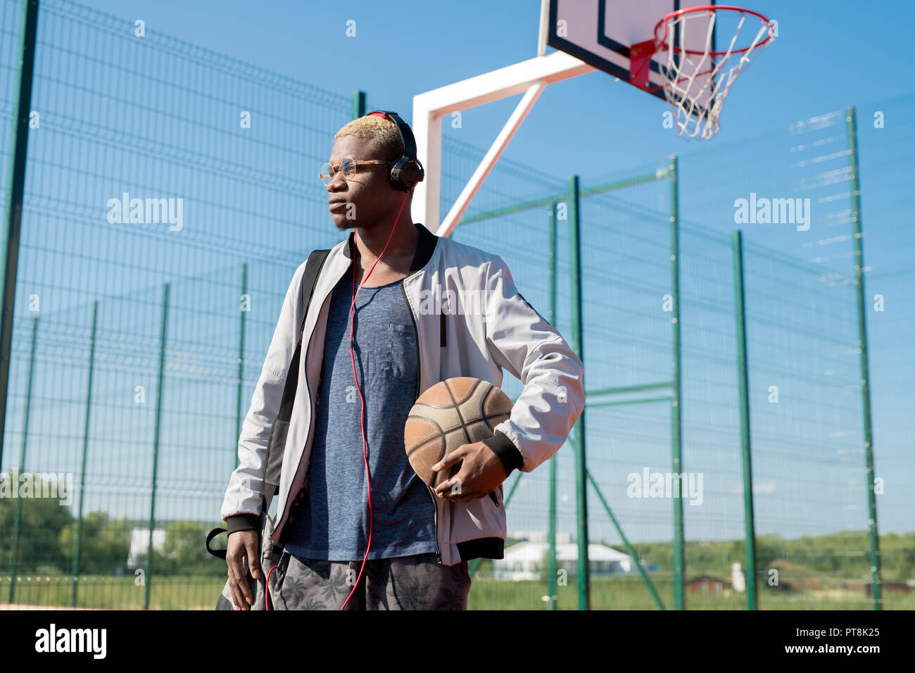 Vita ritratto di africana contemporanea uomo holding basket ball in piedi in corte, spazio di copia Foto Stock